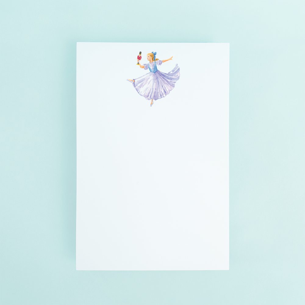 
                  
                    Clara from the nutcracker ballet holding a nutcracker watercolor design on a notepad.
                  
                