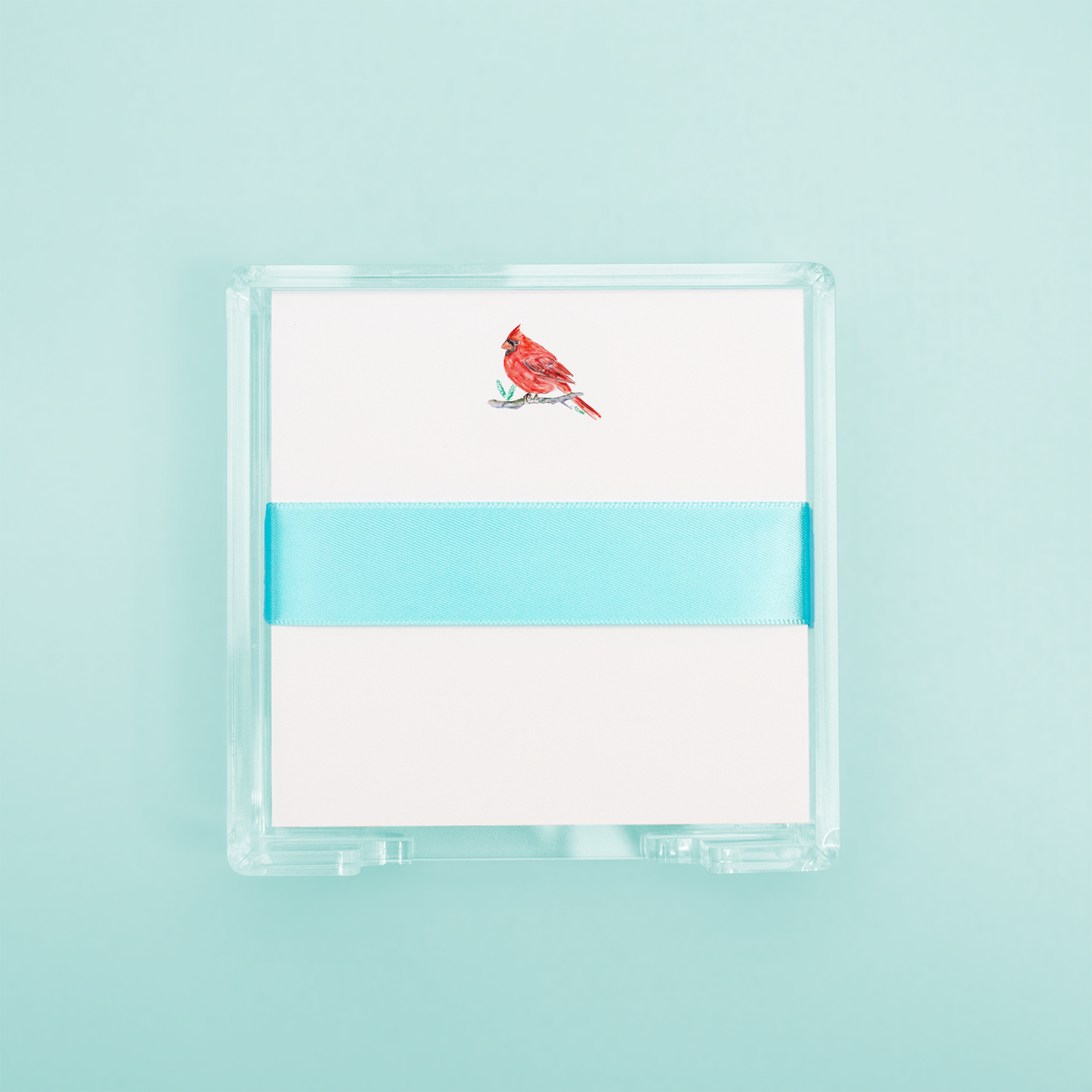 A notepad with a watercolor illustration of a red cardinal bird on a white background, with an acrylic holder.