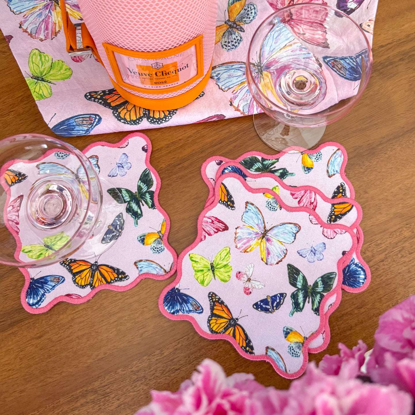 Bottle of champagne featuring butterfly coasters, accompanied by a coupe champagne glass on a wooden surface with flowers.