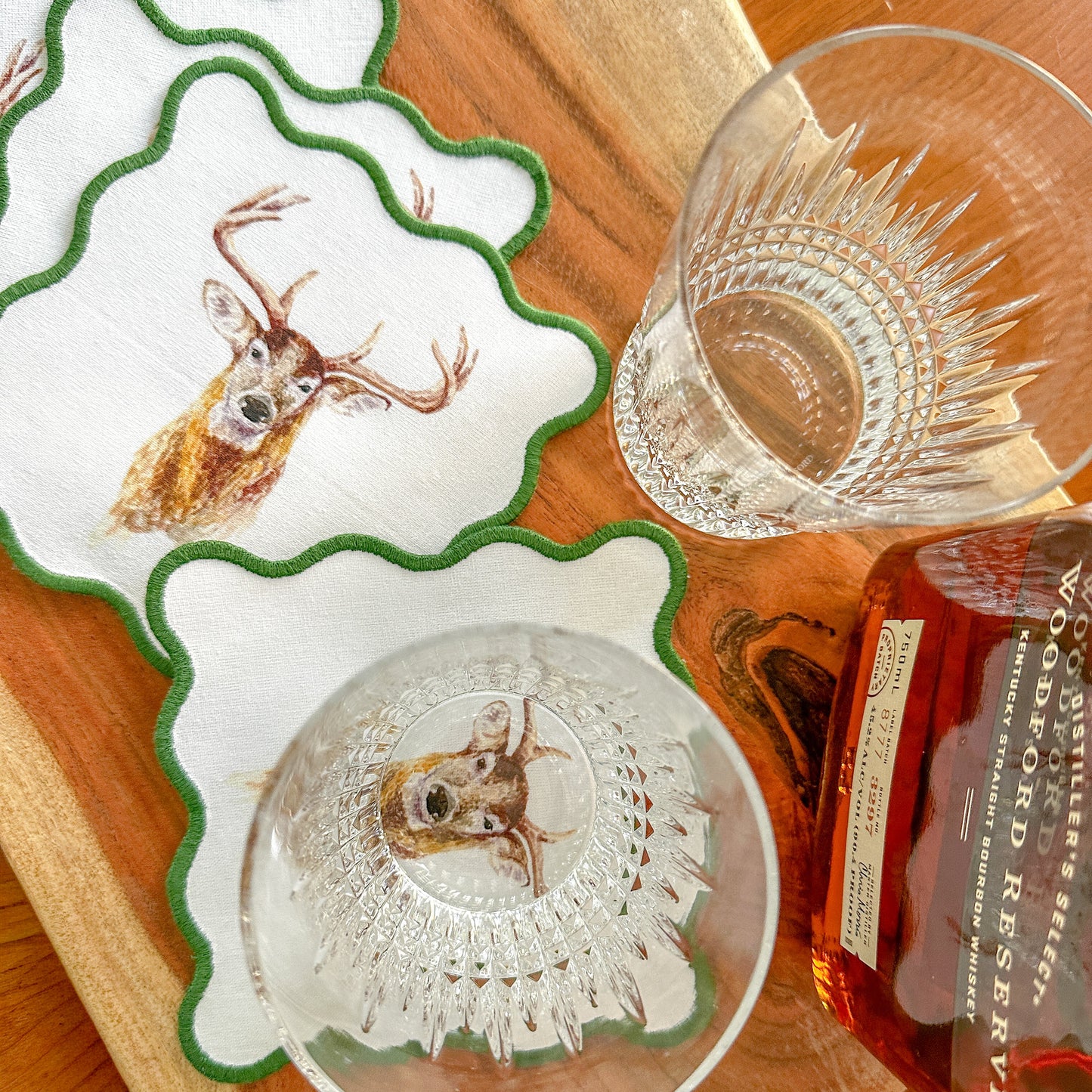Coasters with deer design on a wooden surface with a bottle of whiskey.