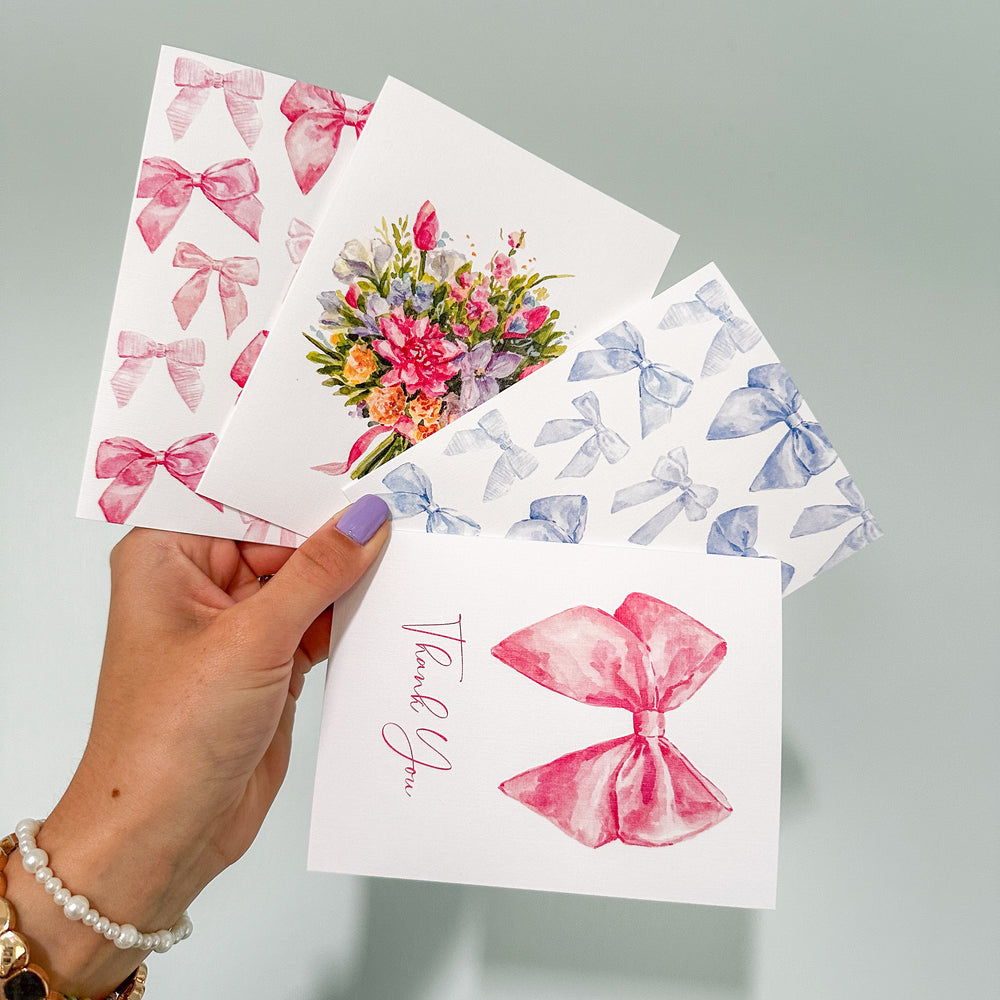 a hand holding up 4 cards. One with pink bows, one with blue bows, one bouquet tied together with a bow, and a bow thank you card.