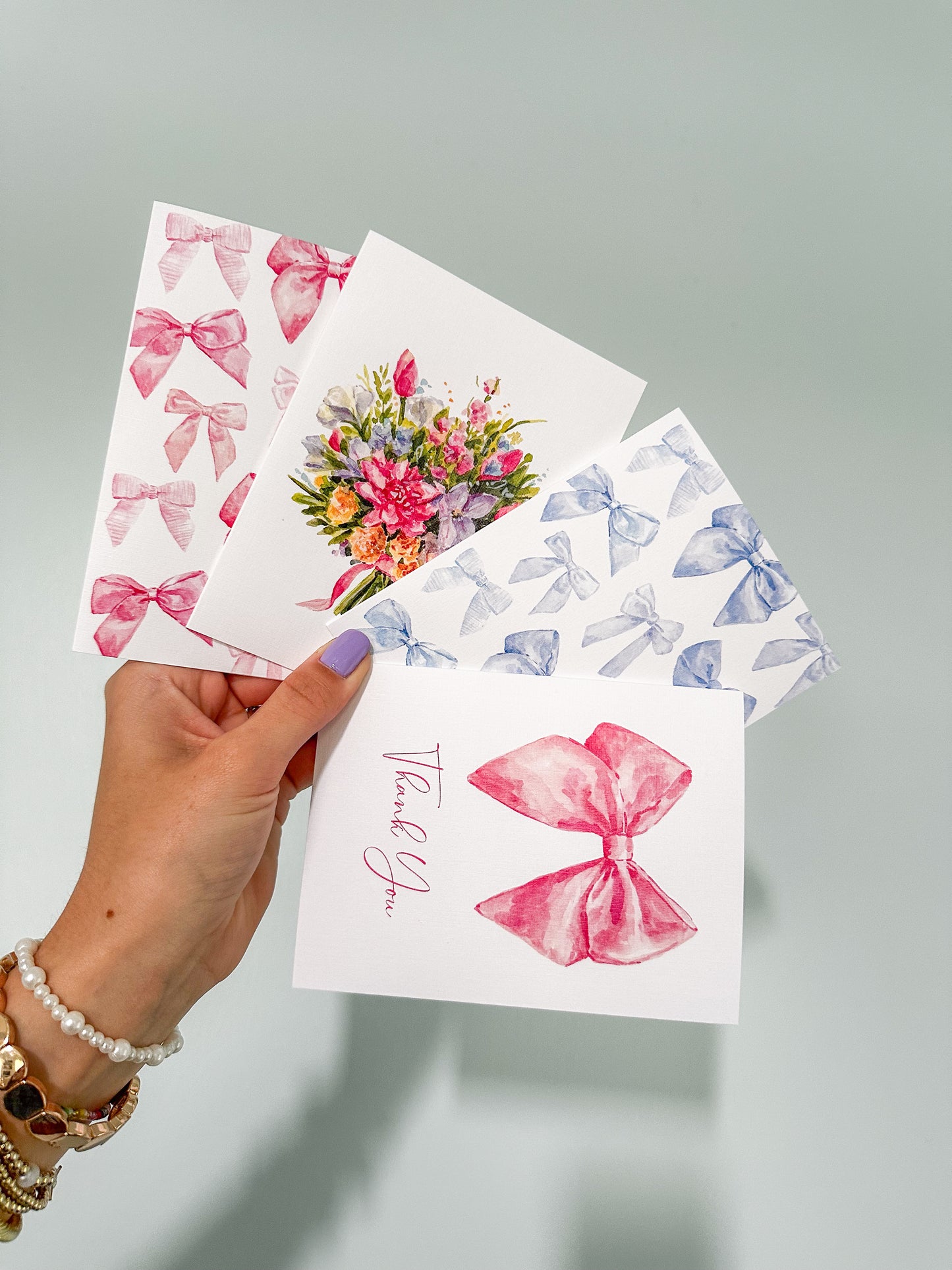 a hand holding up 4 cards. One with pink bows, one with blue bows, one bouquet tied together with a bow, and a bow thank you card.