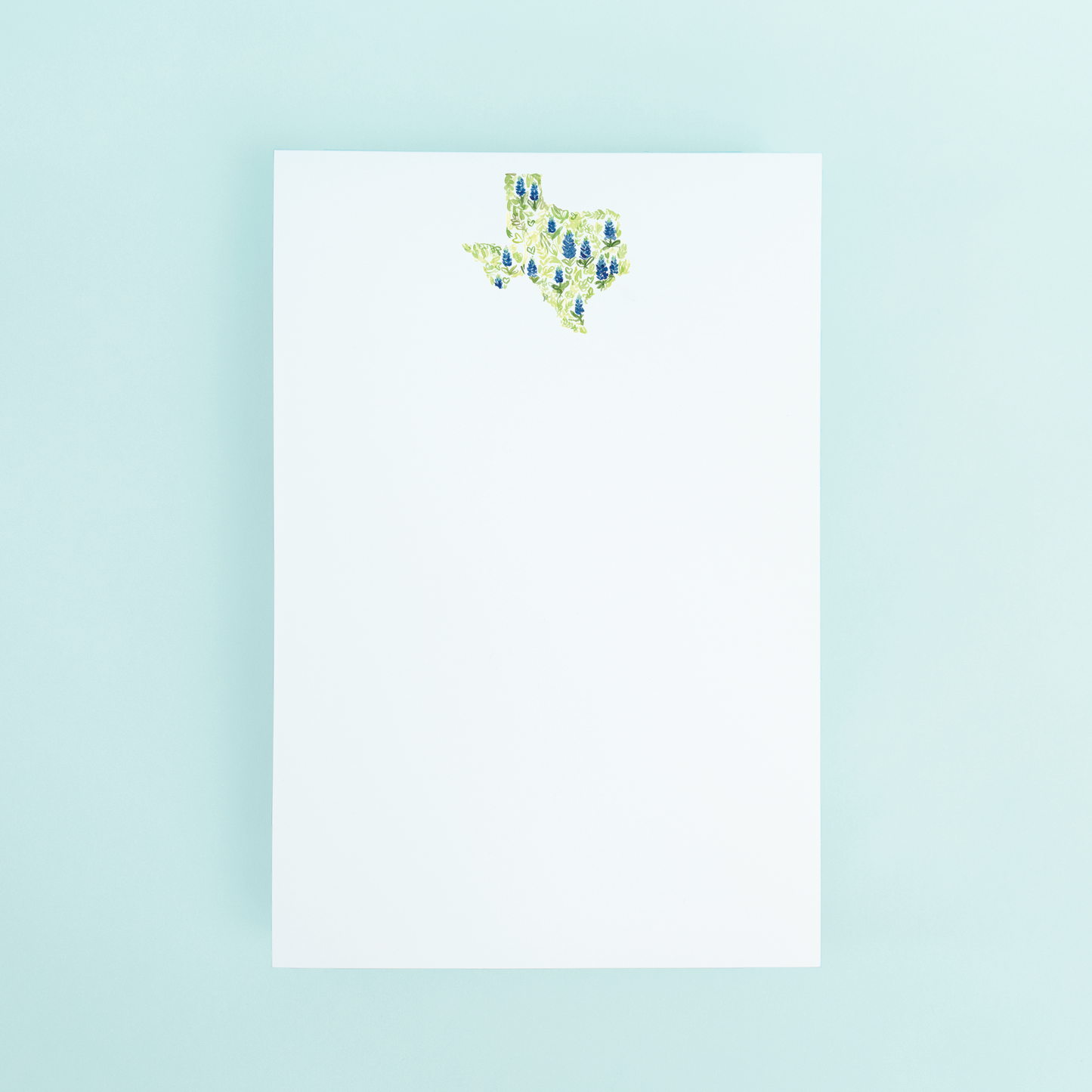 A notepad with a watercolor illustration of the state of Texas filled with bluebonnets flowers on a white background.
